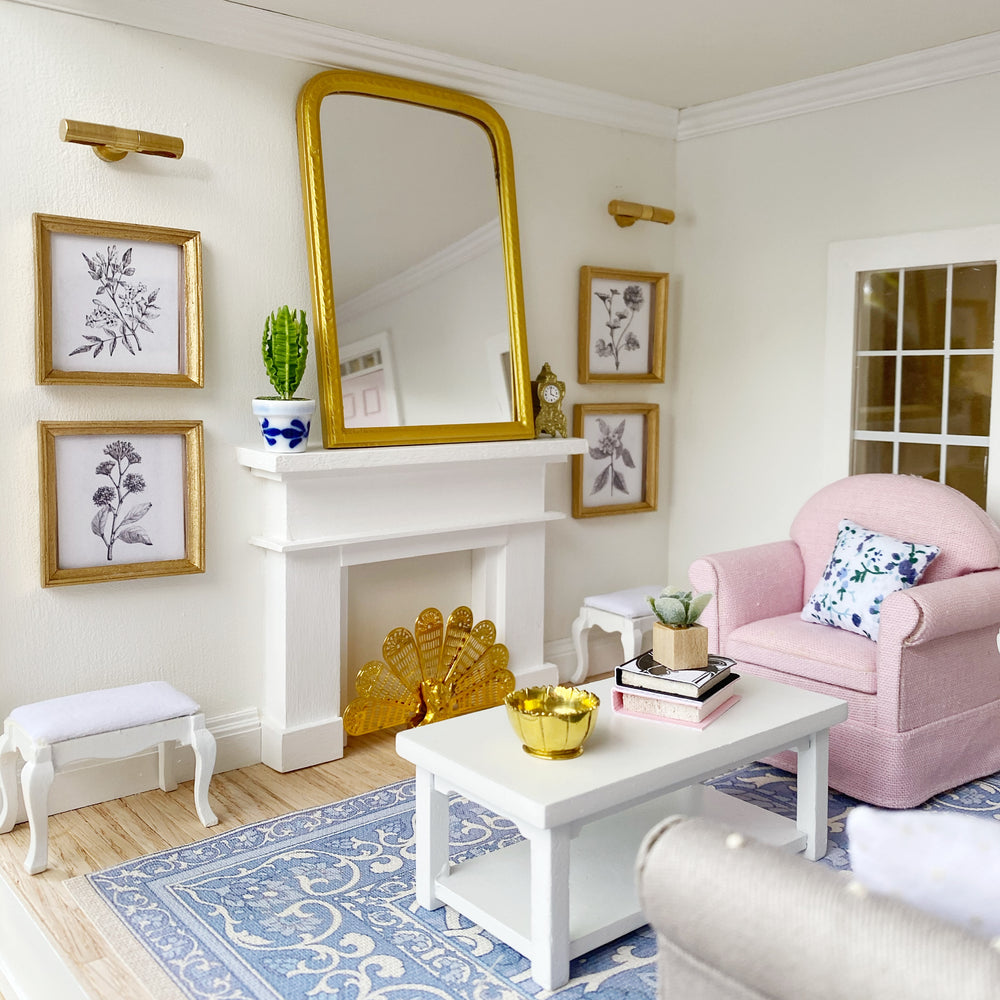 A 1:12 scale sitting room with a gold mirror over a white mantel and a pink armchair