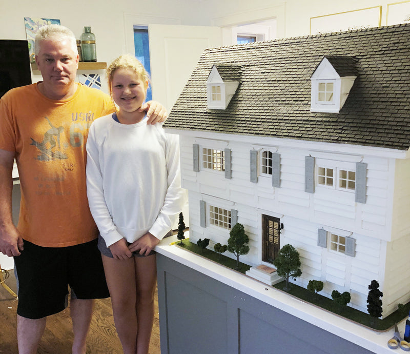 Ella at eleven standing beside her grandpa and the first dollhouse they built together, a white two-storey house with a grey roof